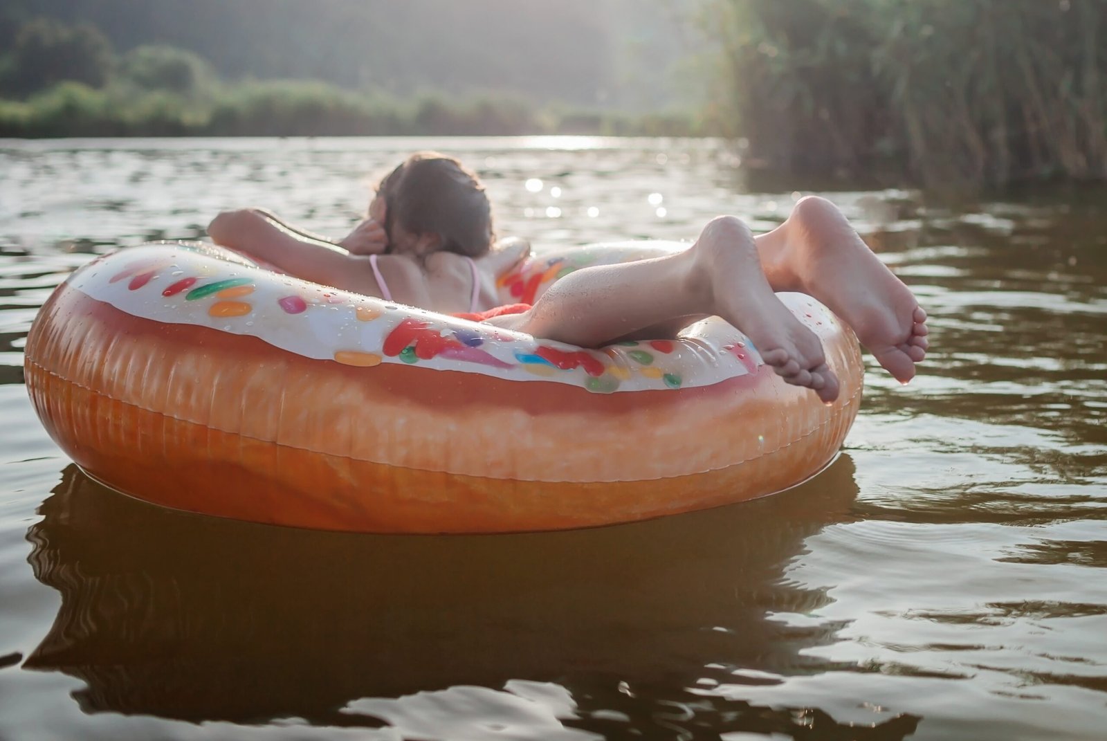 girl relaxes on big donut inflatable ring on lake on hot summer day, happy summertime, countryside